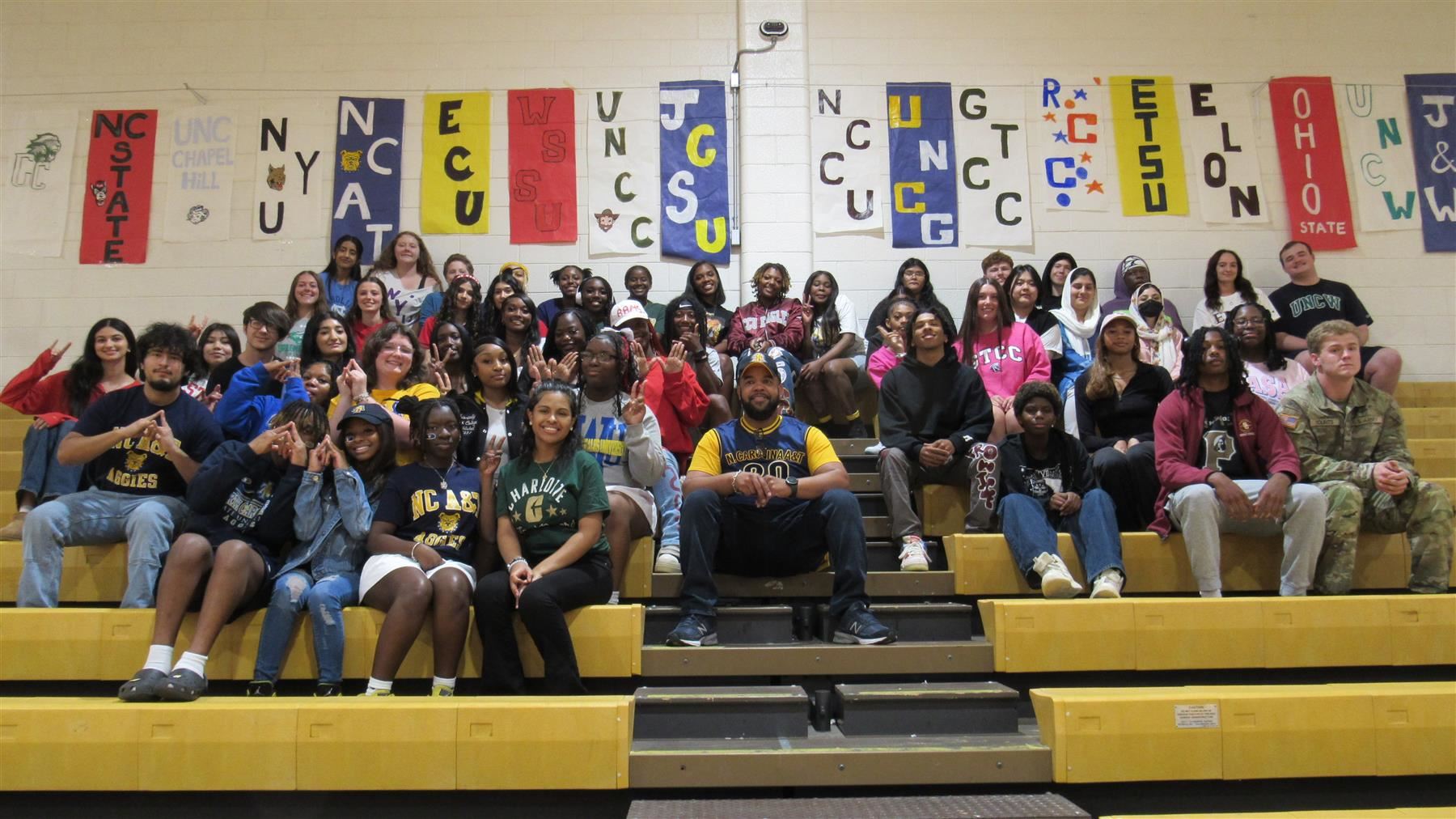 High school students on gym bleachers with college banners in the background